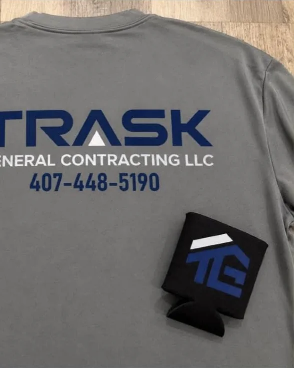 Black can koozie printed with the Trask General Contracting logo, on a matching shirt